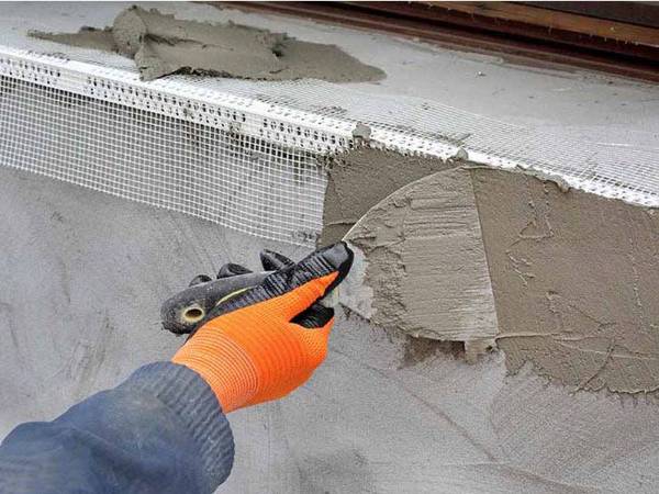 A worker is plastering the window corner with PVC corner bead.